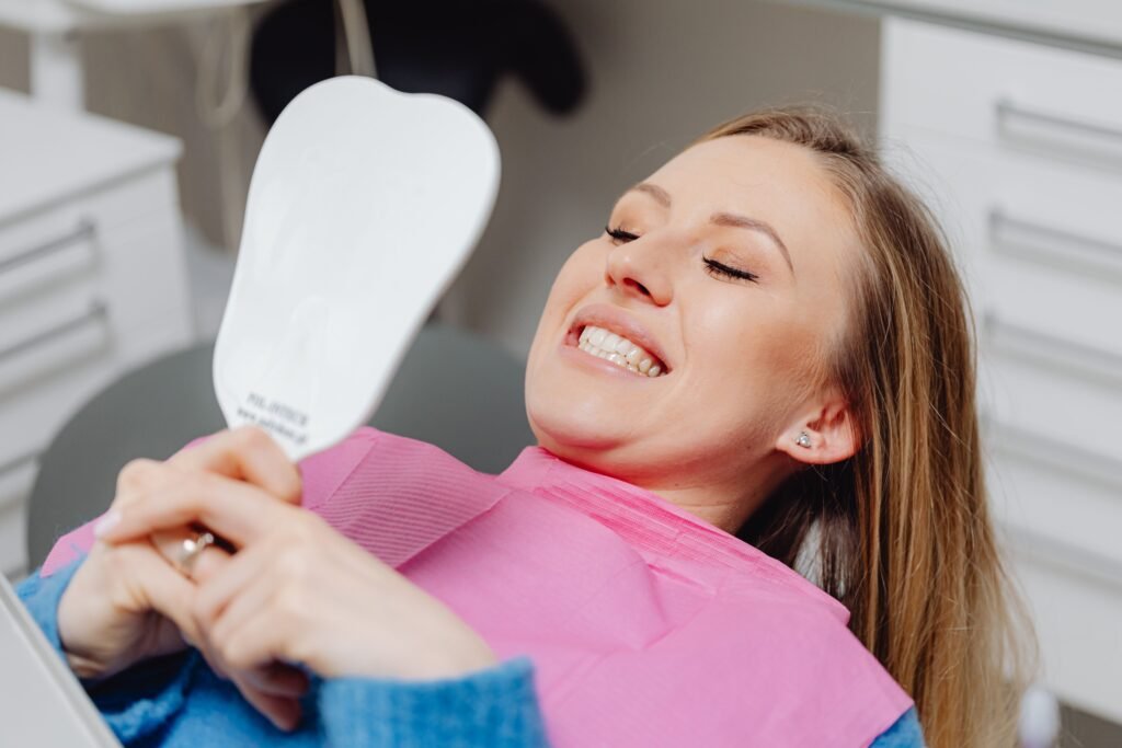 Female patient smiling at her restored smile in a mirror after replacing a missing front tooth in Marshville, NC.